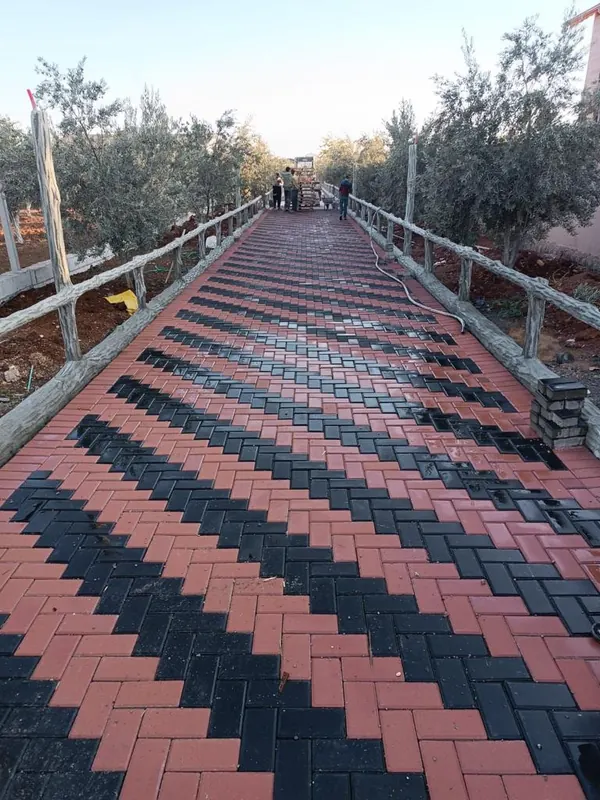 Ağaçlar arasından geçen, kırmızı kilit parke üzerine siyah zikzak desen işlenmiş, iki yanı korkuluklu yürüyüş yolu