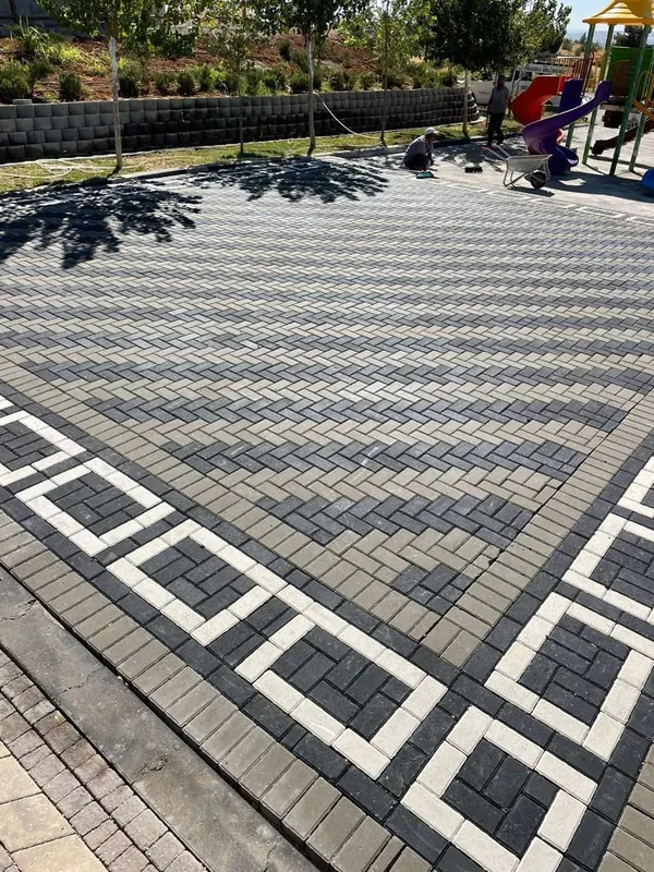 Oyun alanı yanında gri ve siyah balık sırtı kilit parke zemin ile beyaz parkelerle çizilmiş geometrik bordür